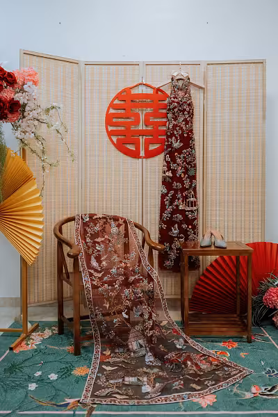Oriental tea ceremony setup with bamboo folding screen, red double-happiness wall decor, pleated fans, and vintage floral carpet