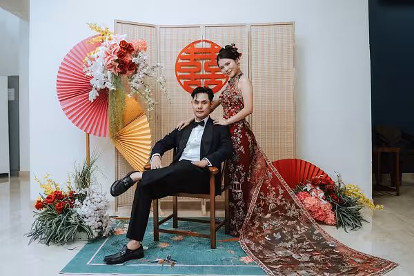 Oriental Chinese tea ceremony setup with bamboo screen, red double-happiness wall decor, pleated fans, and floral arrangements