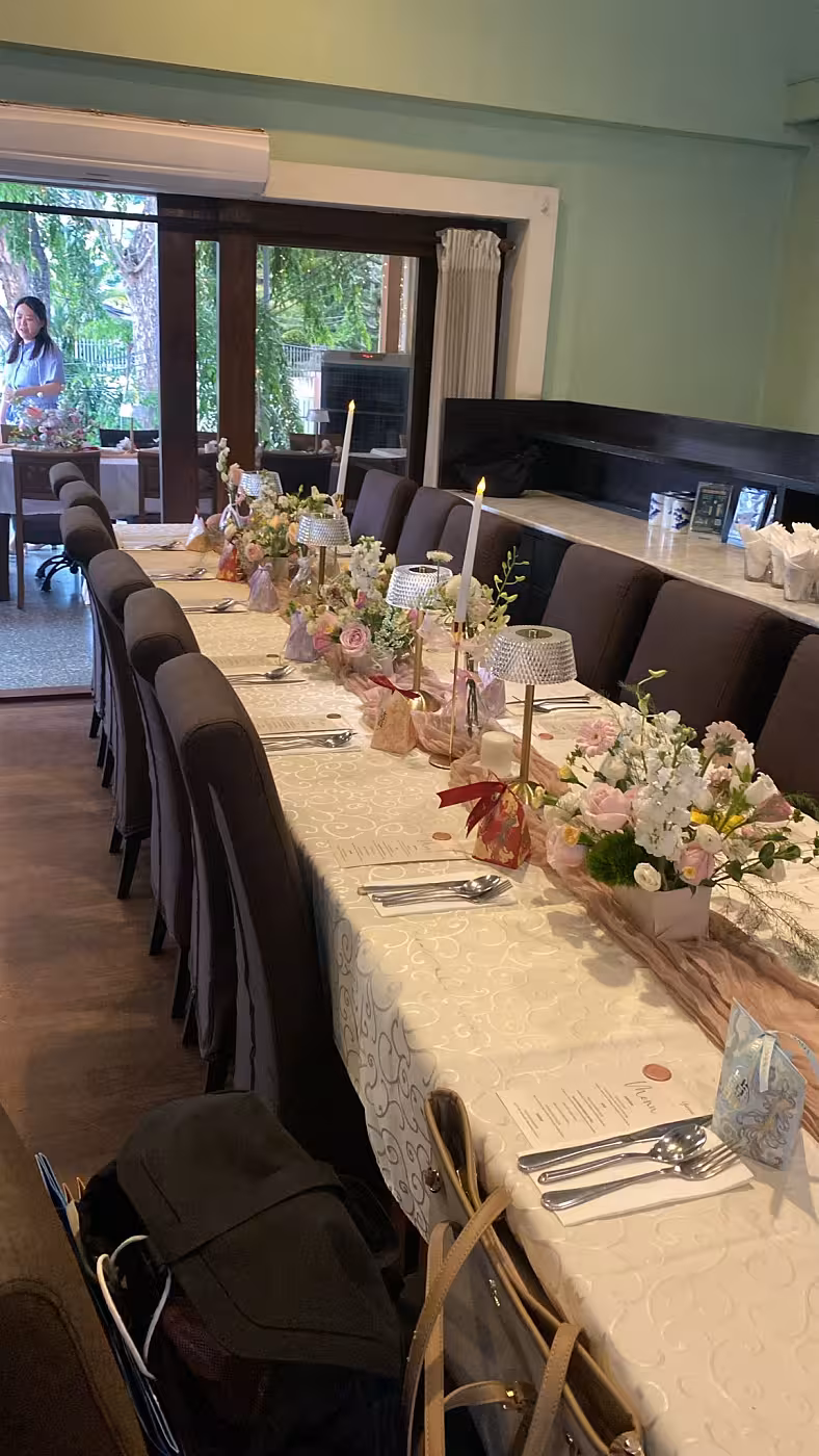 A long dining table is dressed with a soft pink Crumpled Table Runner layered over a white patterned tablecloth, anchored by clusters of pink and white blooms. Crystal Shade Portable Dining Table Lamps in gold and tall taper candles add a warm, romantic glow to the intimate tablescape.