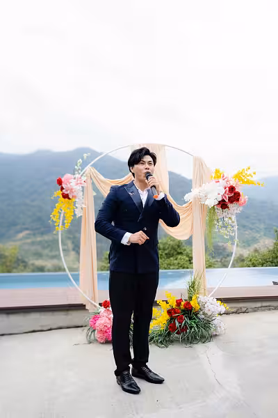 White 2m round arch backdrop draped in beige fabric with red, pink, yellow, and white artificial flower arrangements at sides and base