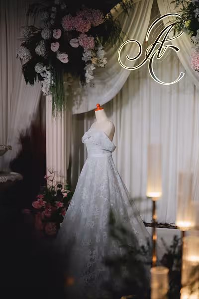 Foam layered mannequin with wooden pole displaying a white lace gown against a draped backdrop with pink floral arch and neon monogram
