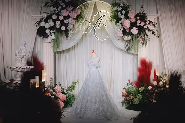 Foam layered mannequin displaying a lace gown before a circular floral arch with pink blooms and neon monogram
