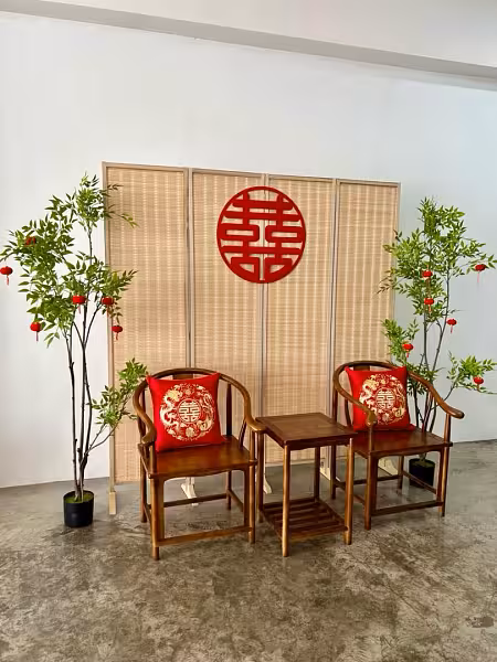 Four-panel bamboo folding screen with red double-happiness wall decor, walnut chairs with dragon-phoenix cushions, and nandina trees with hanging red lanterns