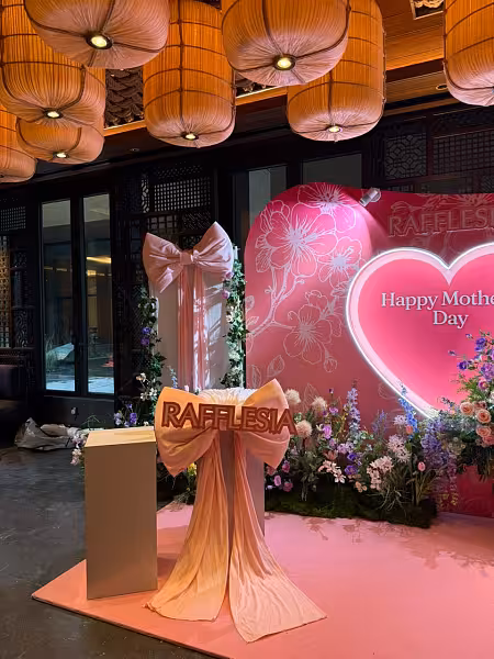 Pink floral backdrop with neon heart sign, giant decorative bow ribbons, white iron cuboid dessert stands, and garden flower clusters