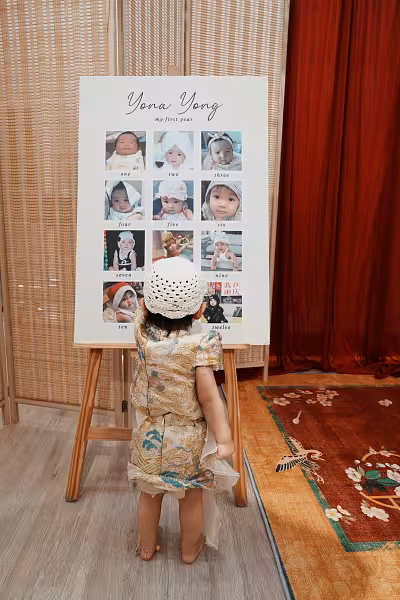Tall wooden easel stand displaying a cream milestone photo board with script typography and monthly photo grid