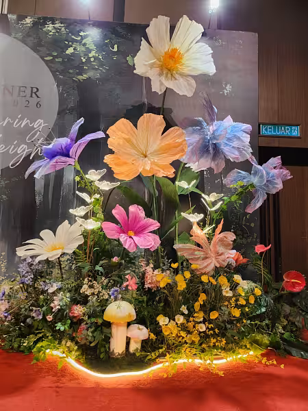Oversized paper flowers in white, peach, pink, purple and blue rising from a lush garden display with glowing butterfly LED walkway lights and mushroom props