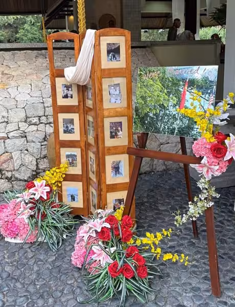 Wooden tri-panel photo display and easel framed by red roses, pink hydrangeas, lilies, and yellow florals
