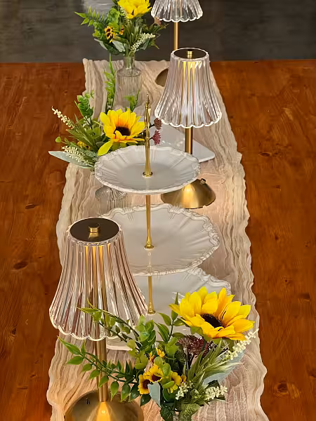 Cream crumpled table runner styled with acrylic crystal LED lamps, a white 3-tier ceramic dessert tray, and sunflower arrangements on a wooden table