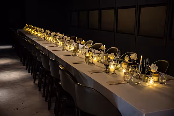 Long banquet table dressed with white artificial rose bouquets, LED taper candles in glass pedestal holders, and glowing crystal tealight cups