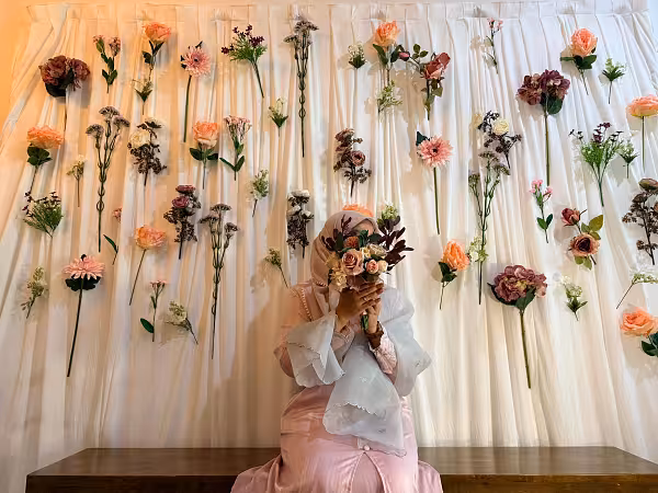 White celebration curtain backdrop adorned with scattered peach, mauve, and cream artificial flowers and greenery