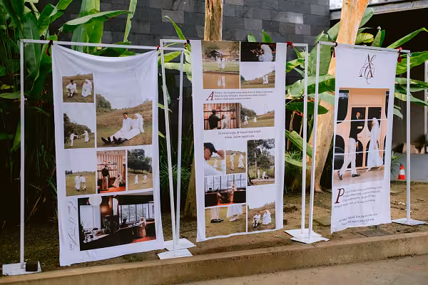 Three white square metal stand arches holding large printed photo collage banners outdoors against lush tropical greenery