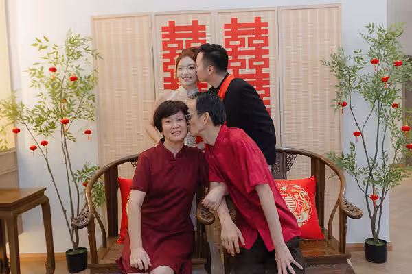 Oriental bamboo folding partition with red double happiness wall decor, flanked by artificial nandina trees with mini red lanterns, and dark walnut chairs with embroidered dragon and phoenix cushions
