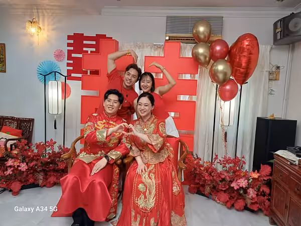 Large red 囍 Double Happiness backdrop flanked by retro arch lantern floor lamps, red artificial blooms, and gold and red balloons