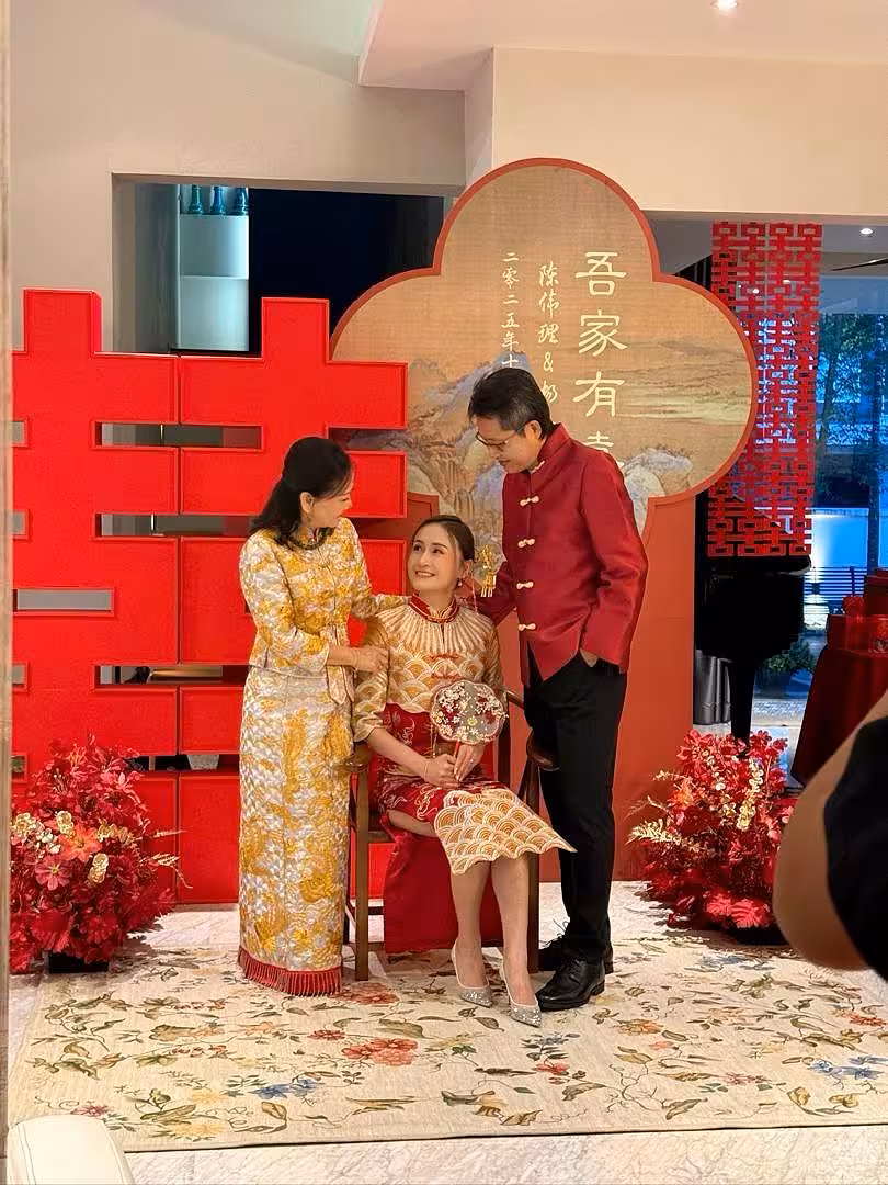A bold 2-metre red 囍 Double Happiness backdrop anchors this traditional Chinese wedding vignette, flanked by lush red artificial floor flowers. A rustic walnut wooden chair dressed with embroidered Dragon and Phoenix cushion covers completes the richly styled, auspicious setting.
