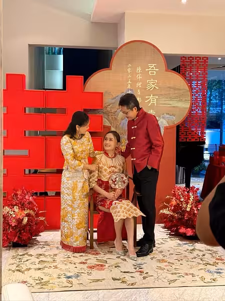 Large red 囍 Double Happiness backdrop with rustic wooden chair, embroidered cushion covers, and red artificial floor flowers