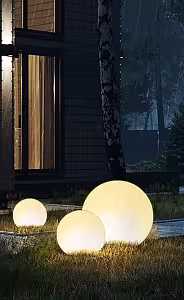 Three LED Ball Stone Sphere Lights glowing warm white in varying sizes on a dark rainy night beside a modern house exterior