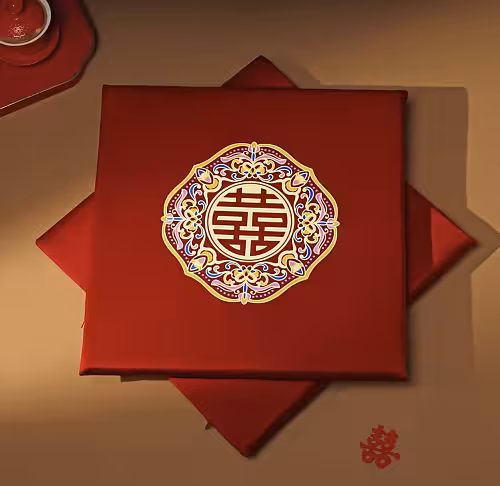 Overhead view of two red satin wedding kneeling pads stacked offset, top cushion showing close-up embroidered double happiness medallion