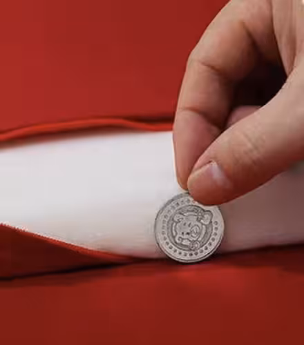 Hand tucking a small silver auspicious coin into the inner white filling of a red satin wedding kneeling cushion