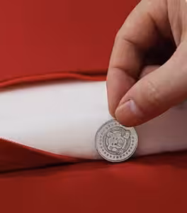 Hand tucking a small silver auspicious coin into the inner white filling of a red satin wedding kneeling cushion
