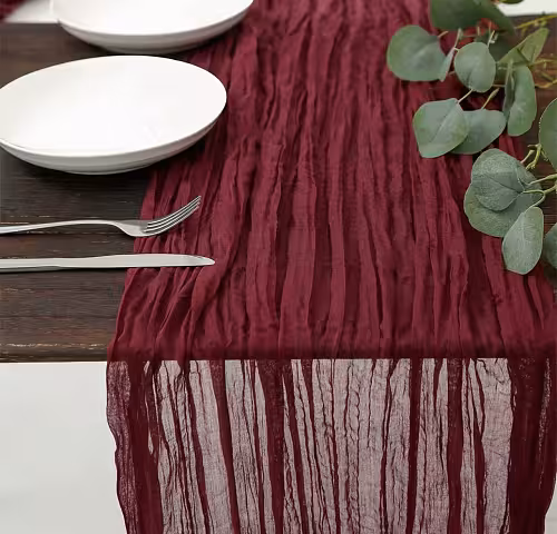 Maroon Crumpled Table Runner on a dark wood table with white plates, silver cutlery, and eucalyptus, its sheer end draping off the edge