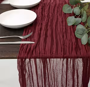 Maroon Crumpled Table Runner on a dark wood table with white plates, silver cutlery, and eucalyptus, its sheer end draping off the edge