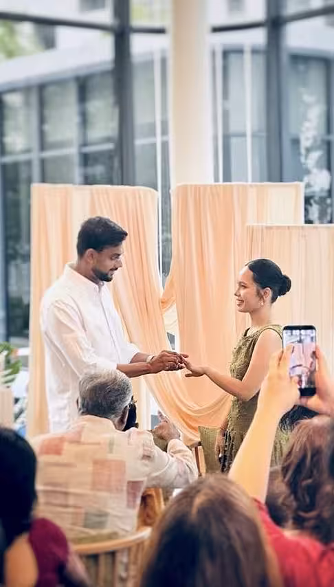 Soft champagne-toned stretchable drape fabric panels are arranged in layered columns to form an elegant backdrop, creating a warm, airy ambience against large glass windows. The lightweight fabric catches natural light beautifully, lending a refined and intimate feel to the ceremony space.