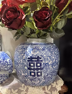 Close-up of the Oriental Blue and White Floral Pattern Round XI Vase holding deep red roses on a lace doily, with a lidded jar beside it