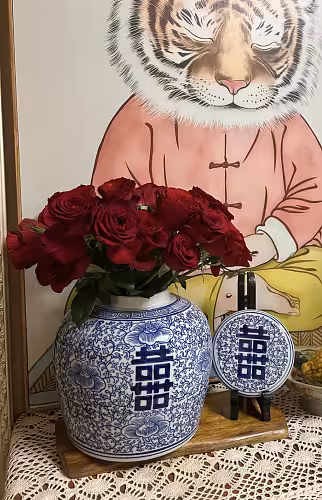 Oriental Blue and White Floral Pattern Round XI Vase filled with red roses on a lace runner, in front of a framed tiger art print