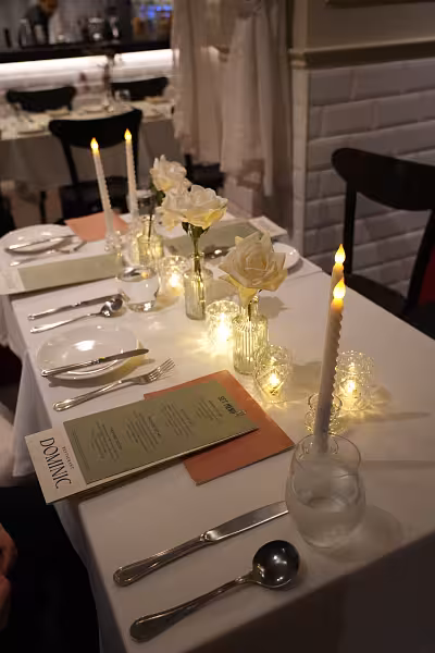 White artificial roses in mini clear glass vases with LED spiral taper candles and crystal tealight cups on a white dining table