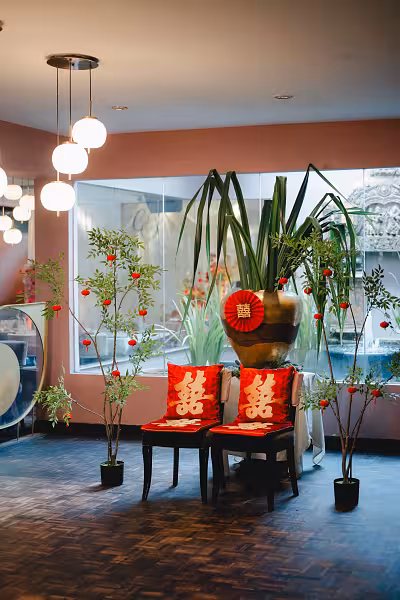 Artificial potted nandina trees dotted with small red velvet hanging lanterns flanking two chairs with red double happiness cushions