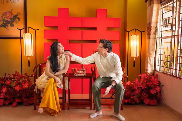 Bold red 囍 Double Happiness backdrop flanked by vertical lantern floor lamps and red artificial flowers, with rustic walnut wooden chair and table set