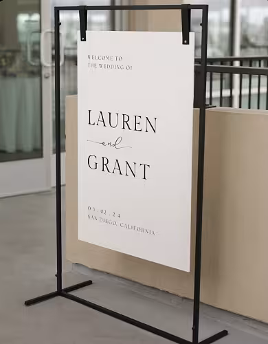 Black Rectangle Decorative Screen Arches Frame displayed at a slight angle, holding a minimalist white wedding welcome board in an indoor venue