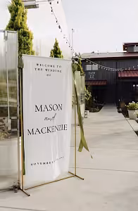 Gold Rectangle Decorative Arch Frame styled outdoors displaying a white wedding welcome banner with green ribbon accents at a farm venue