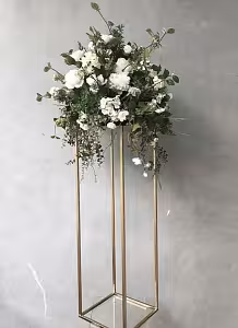 Gold Iron Decorative Event Stand 80 cm topped with a lush white bloom and trailing greenery arrangement against a grey concrete wall