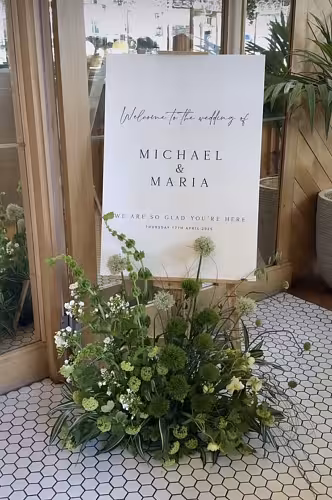 Wooden Easel Stand 175 cm displaying a white wedding welcome sign, framed by a lush green floral arrangement at a bright venue entrance
