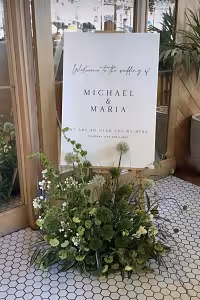 Wooden Easel Stand 175 cm displaying a white wedding welcome sign, framed by a lush green floral arrangement at a bright venue entrance