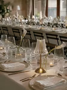 Wireless Acrylic Crystal LED Table Lamp on a gold brass base centrepiece along a long white-linen banquet table with gold cutlery and calla lilies