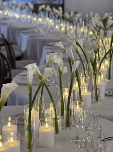 3pc LED Acrylic Candles Set styled on a long white banquet table with white calla lilies, glowing warm yellow among clear acrylic tubes