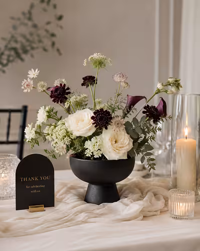 Matte black Pedestal Bowl Vase styled as a wedding centrepiece with cream roses, burgundy blooms, and a Thank You card on a draped table