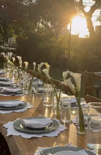 Clear glass cylinder vases holding white calla lilies styled along a wooden outdoor dining table bathed in golden sunset light