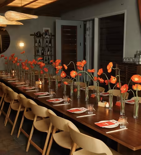 Row of Minimalist Cylinder Clear Glass Vases holding single-stem red poppies lining a long dark wooden restaurant dining table