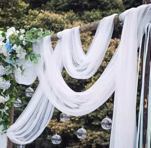 White sheer netted nylon fabric swooped in multi-swag style over a rustic branch arch, with hanging glass orbs and blue-white floral clusters