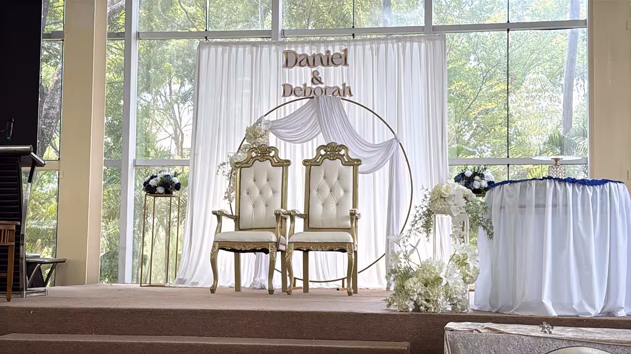 Gold circle backdrop with white draped curtain, artificial white flowers, and gold iron stands on a wedding stage