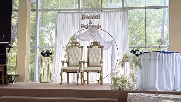 Gold circle backdrop with white draped curtain, artificial white flowers, and gold iron stands on a wedding stage