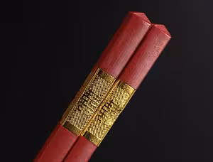 Close-up of two red wooden chopsticks from the Oriental Red Lantern Bowl Set bound by an engraved gold band with Chinese characters