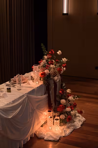 White draped sweetheart table with red and white floral arrangement and glowing crystal rose effect lamps on the floor