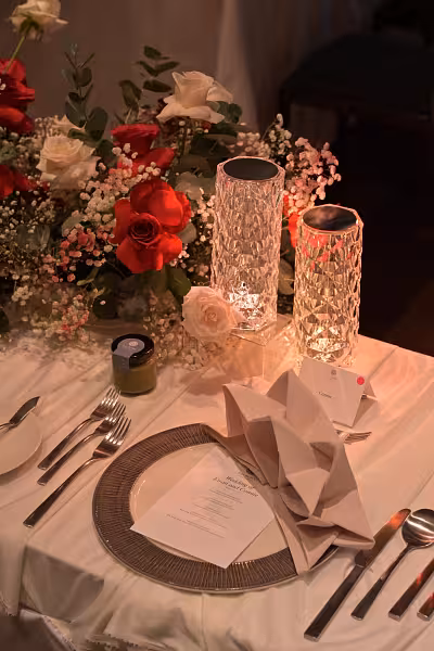 Wedding place setting with two glowing crystal rose effect lamps, red and white floral centrepiece, folded napkin, and heart-shaped menu card