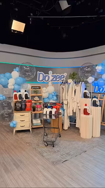 Blue and white balloon garland with oversized clear orb balloons framing a branded studio display featuring pleated cylindrical dessert stands and a wooden easel