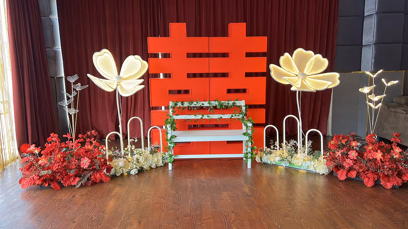 Red 囍 Double Happiness backdrop flanked by butterfly LED walkway lights and red artificial floor flowers with a white bench