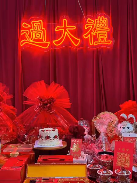 过大礼 neon light sign glowing in gold and red above a wine red velvet curtain backdrop with betrothal gift display
